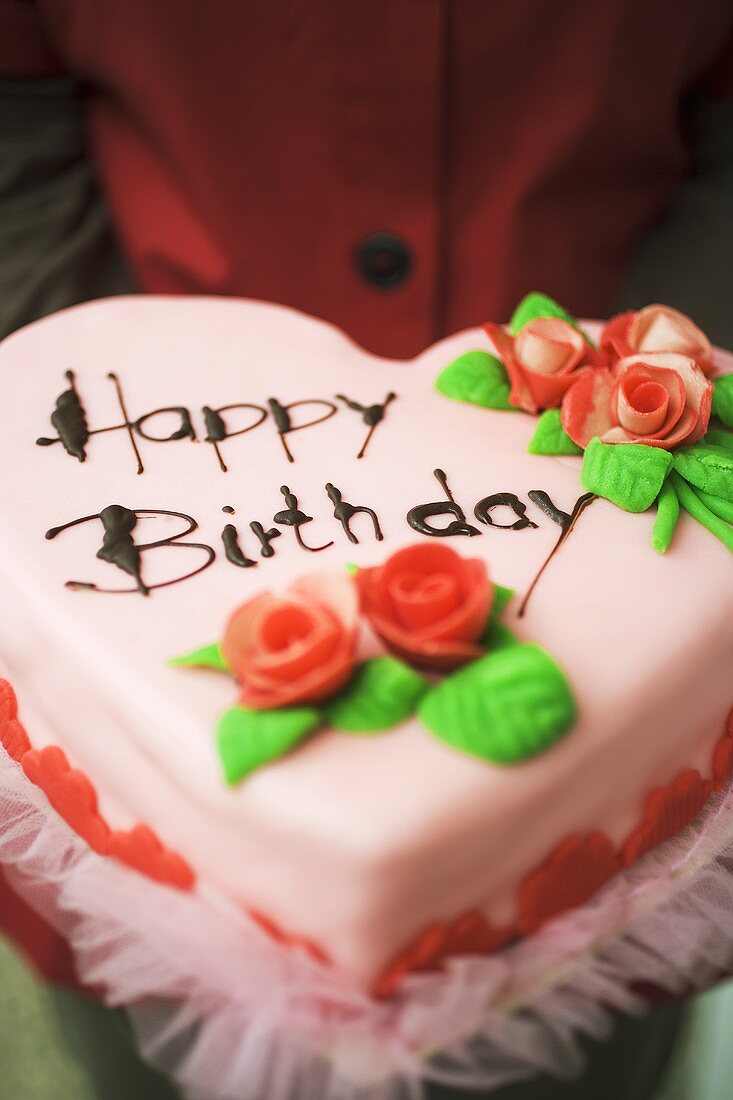 Person holding heart-shaped birthday cake with marzipan roses