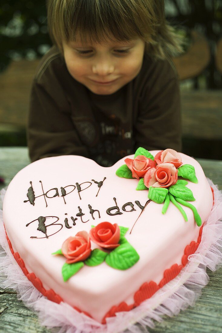 Child with pink heart-shaped birthday cake with marzipan roses
