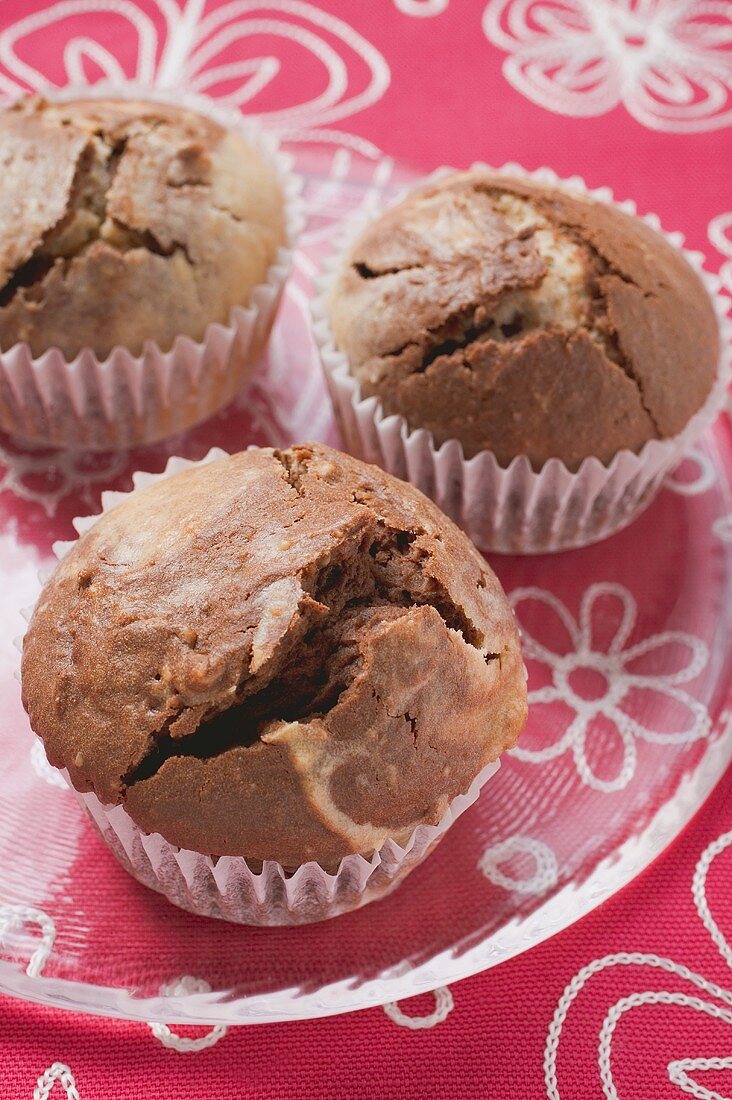 Drei Schoko-Vanille-Muffins in Papierförmchen auf Glasteller