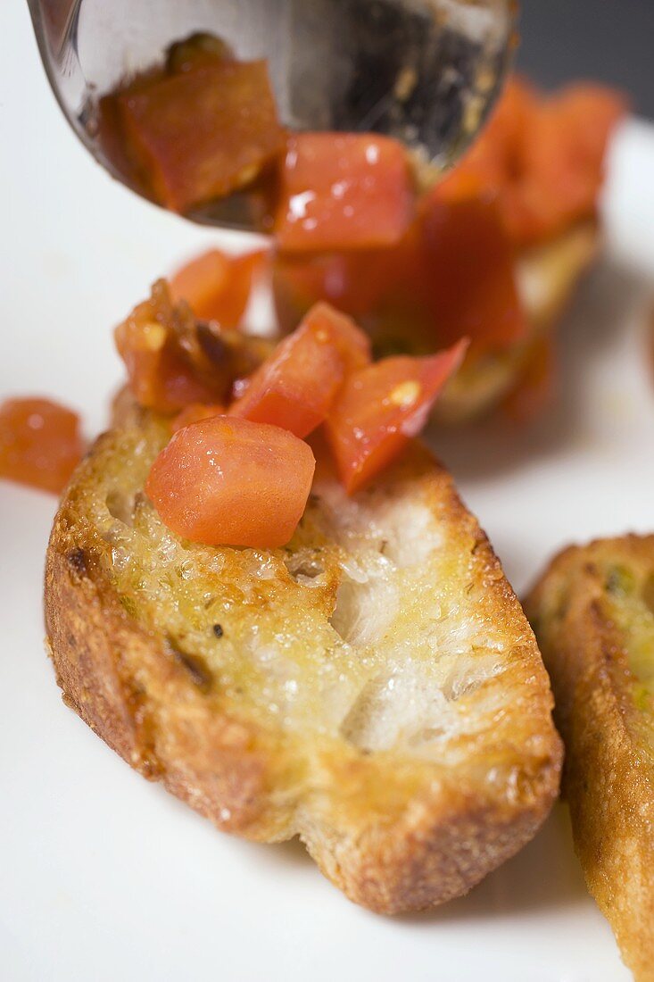 Putting diced tomatoes on toasted baguette slice