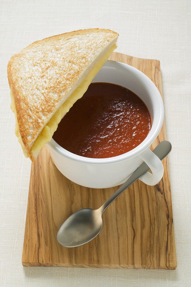 A cup of tomato soup with toasted cheese sandwich on board