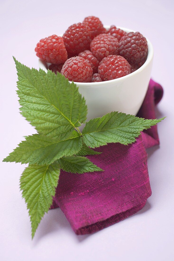 Raspberries in white bowl, raspberry leaves beside it