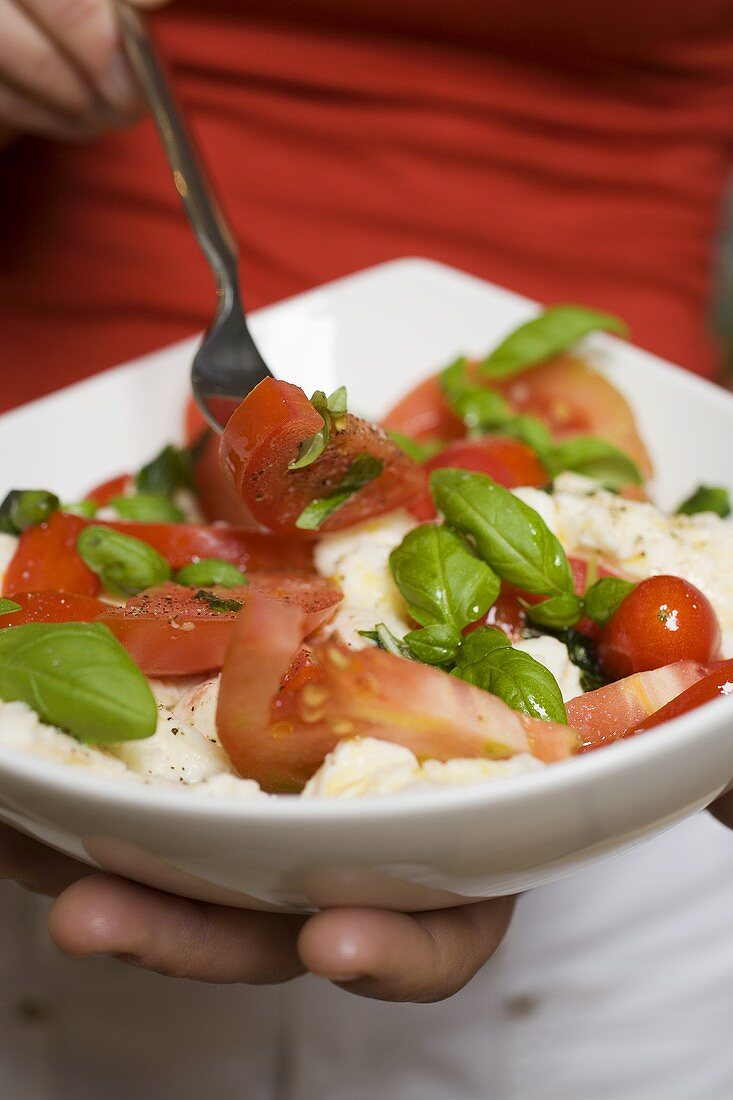 Frau isst Tomaten mit Mozzarella und Basilikum