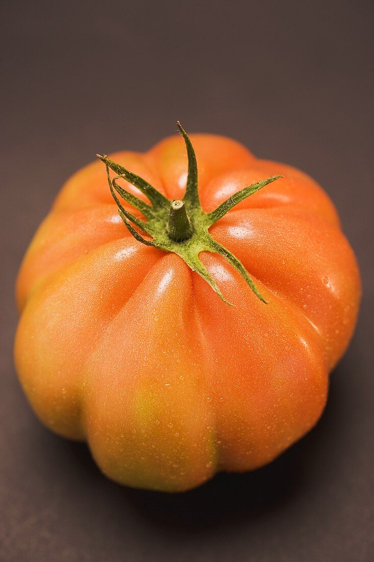 Tomato with drops of water on brown background