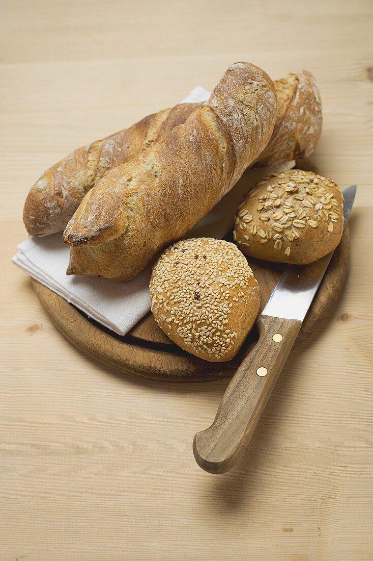 Baguettes and wholemeal rolls on breadboard with knife