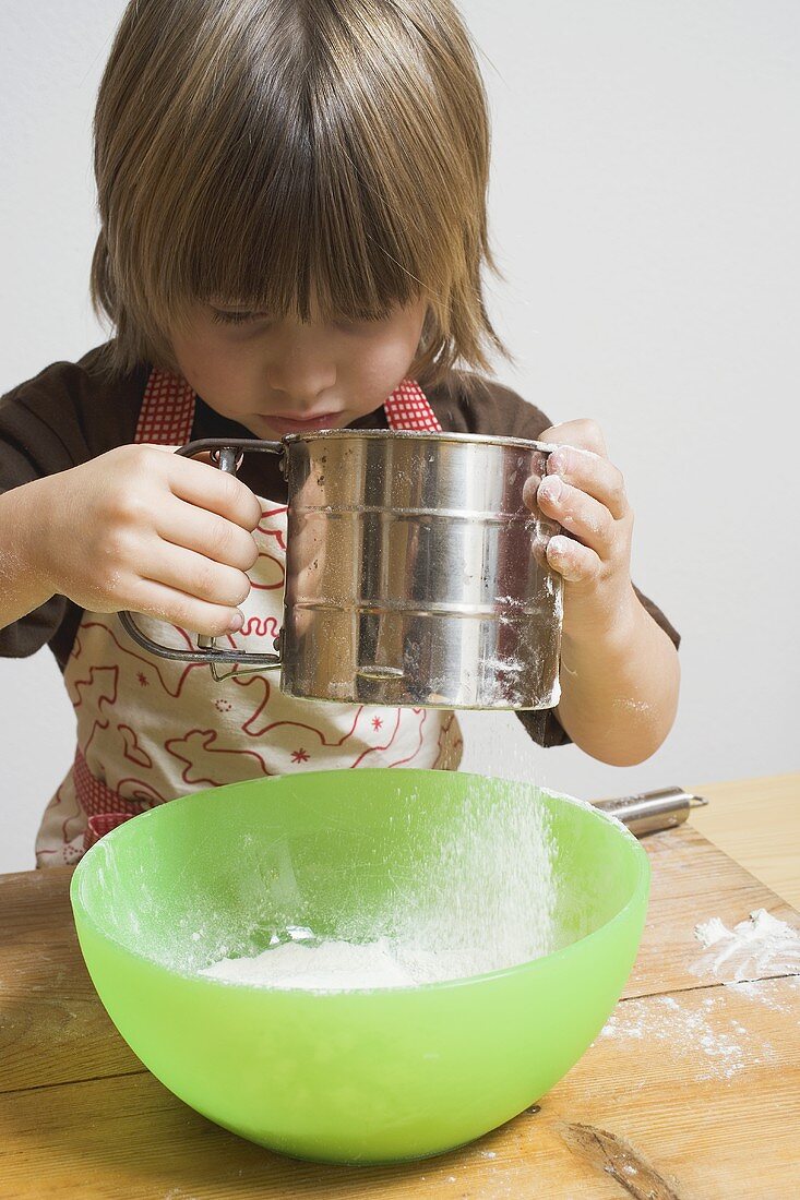 Child sieving flour into a bowl