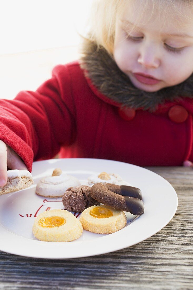 Kleines Mädchen nimmt Weihnachtsplätzchen vom Teller