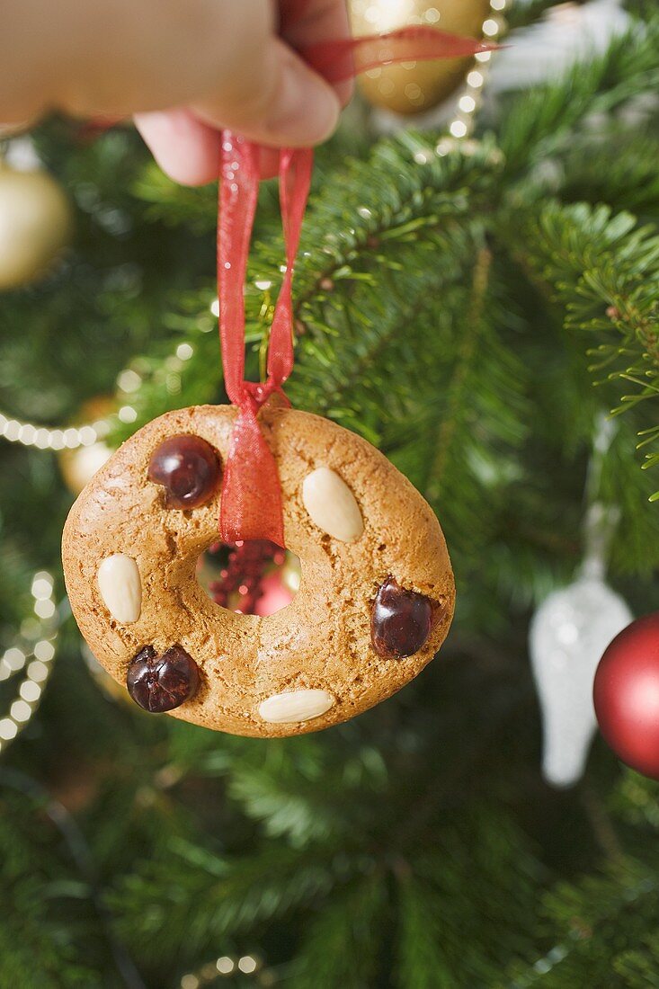 Hand hält Lebkuchenbaumschmuck vor Christbaum