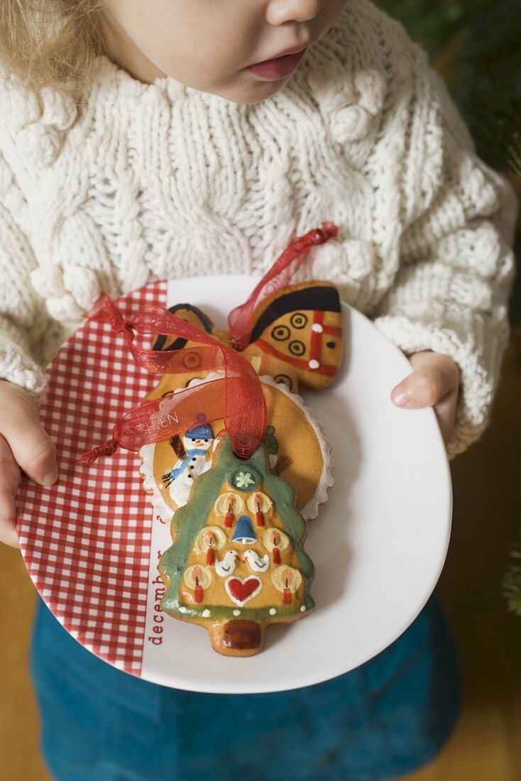 Small girl holding plate of gingerbread tree ornaments