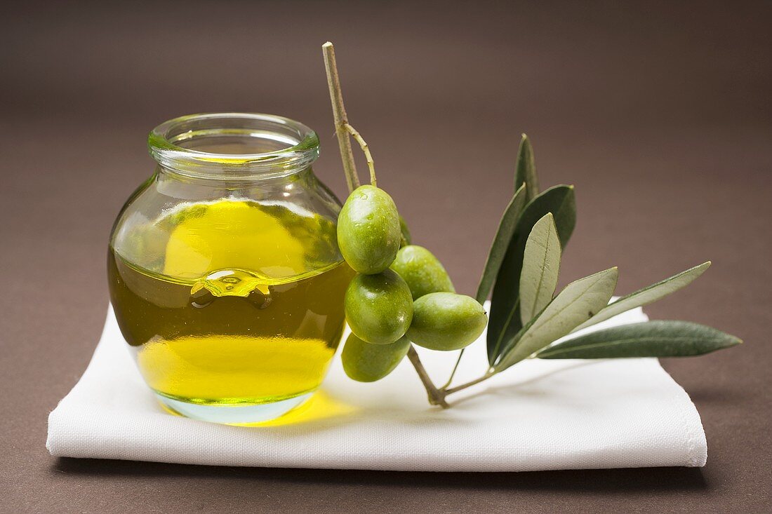 Green olives on twig beside jar of olive oil