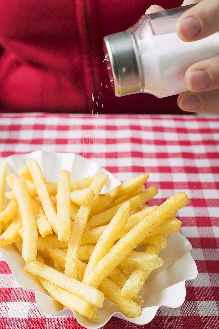 Hand streut Salz auf Pommes frites