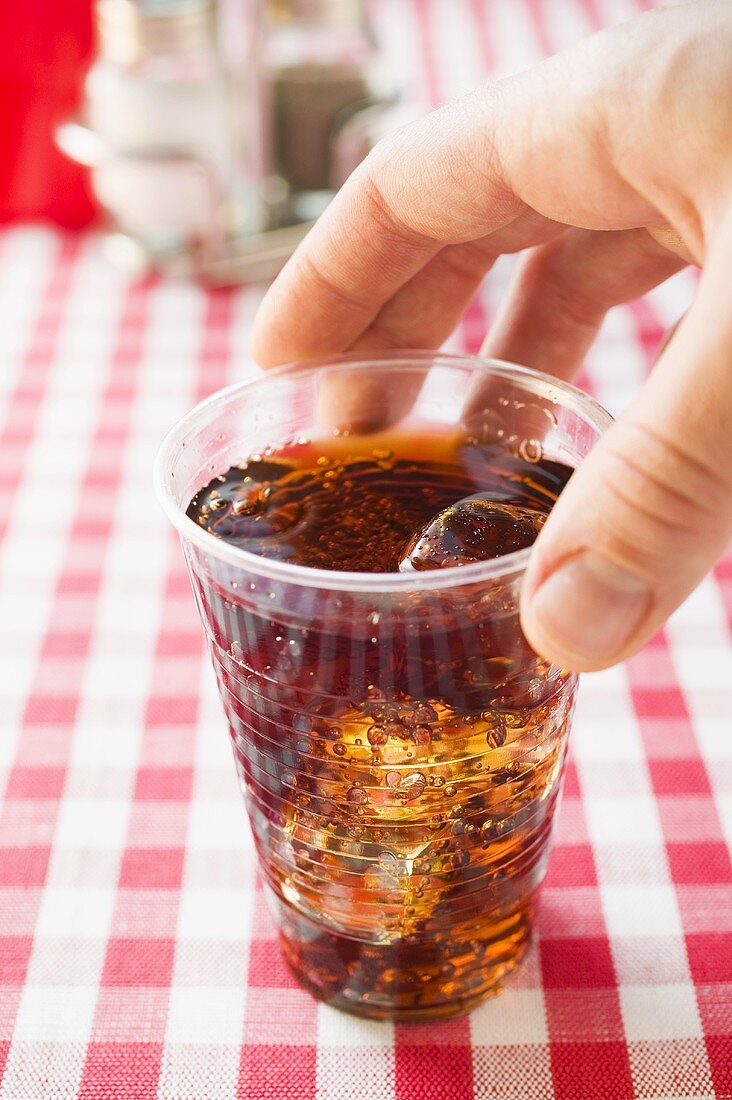 Hand greift nach Cola im Plastikbecher