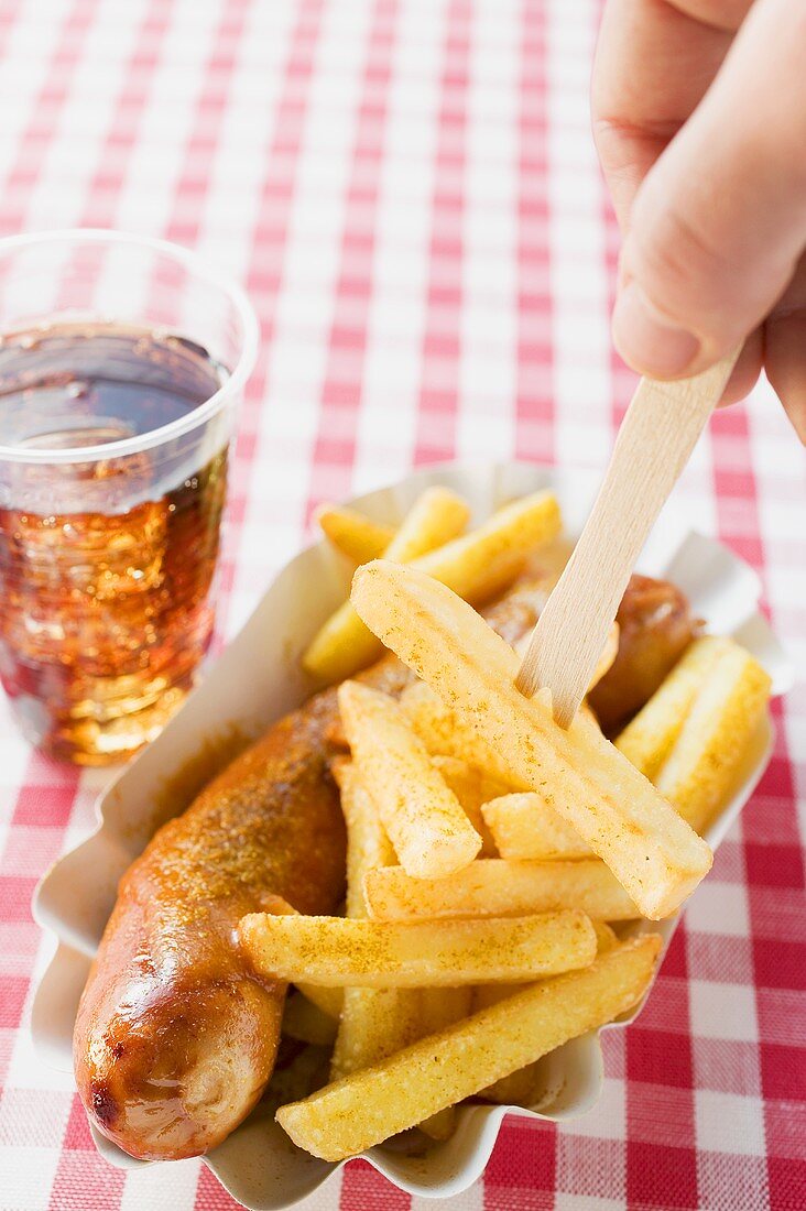 Currywurst with chips, one on wooden fork, and cola