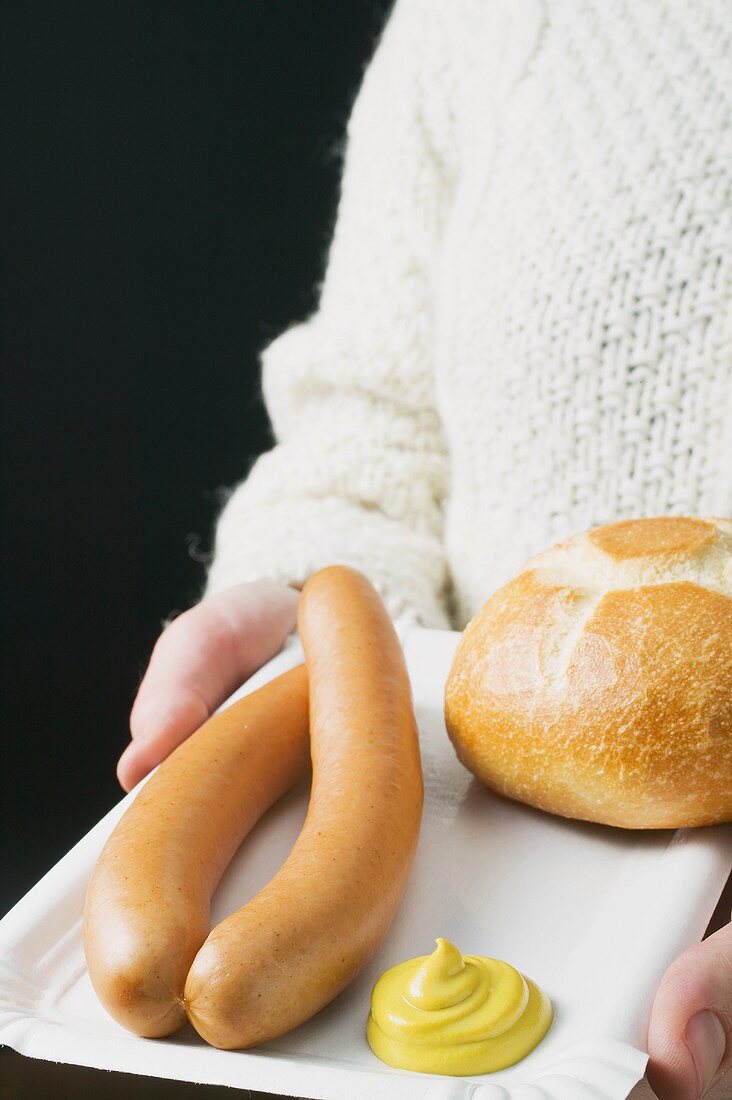 Person hält Pappteller mit Wiener Würstchen, Brötchen, Senf