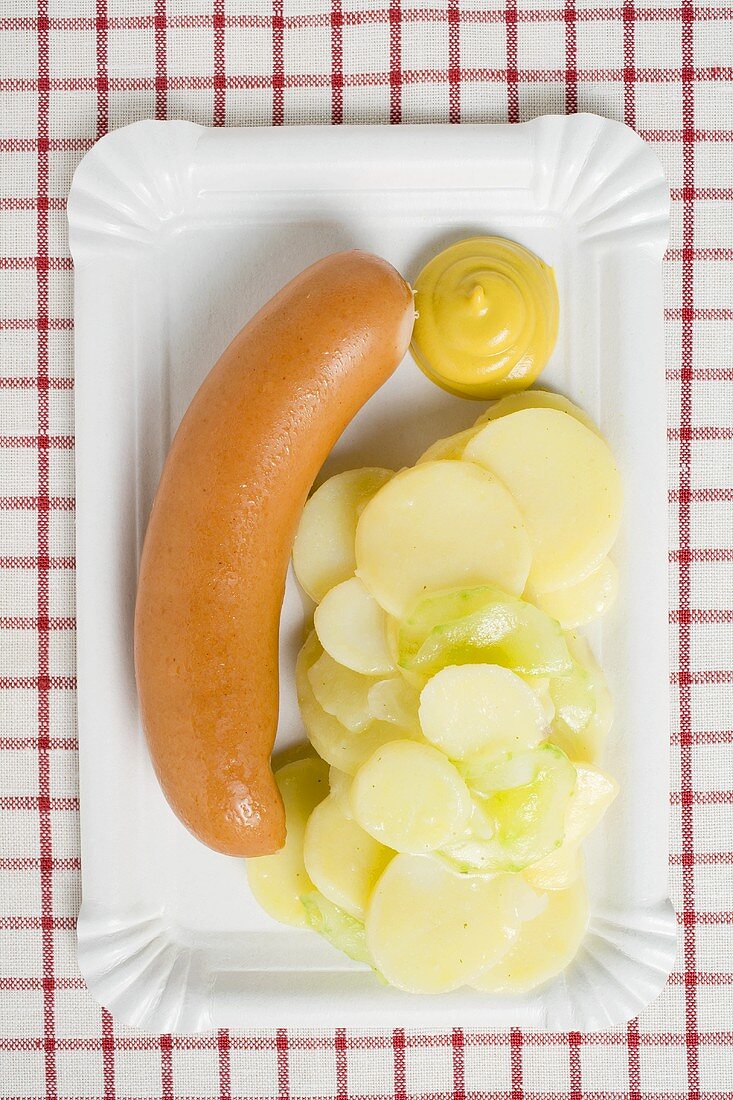 Frankfurter with potato salad and mustard on paper plate