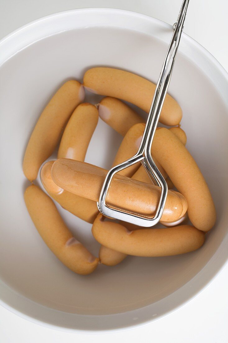 Lifting frankfurters out of water with tongs