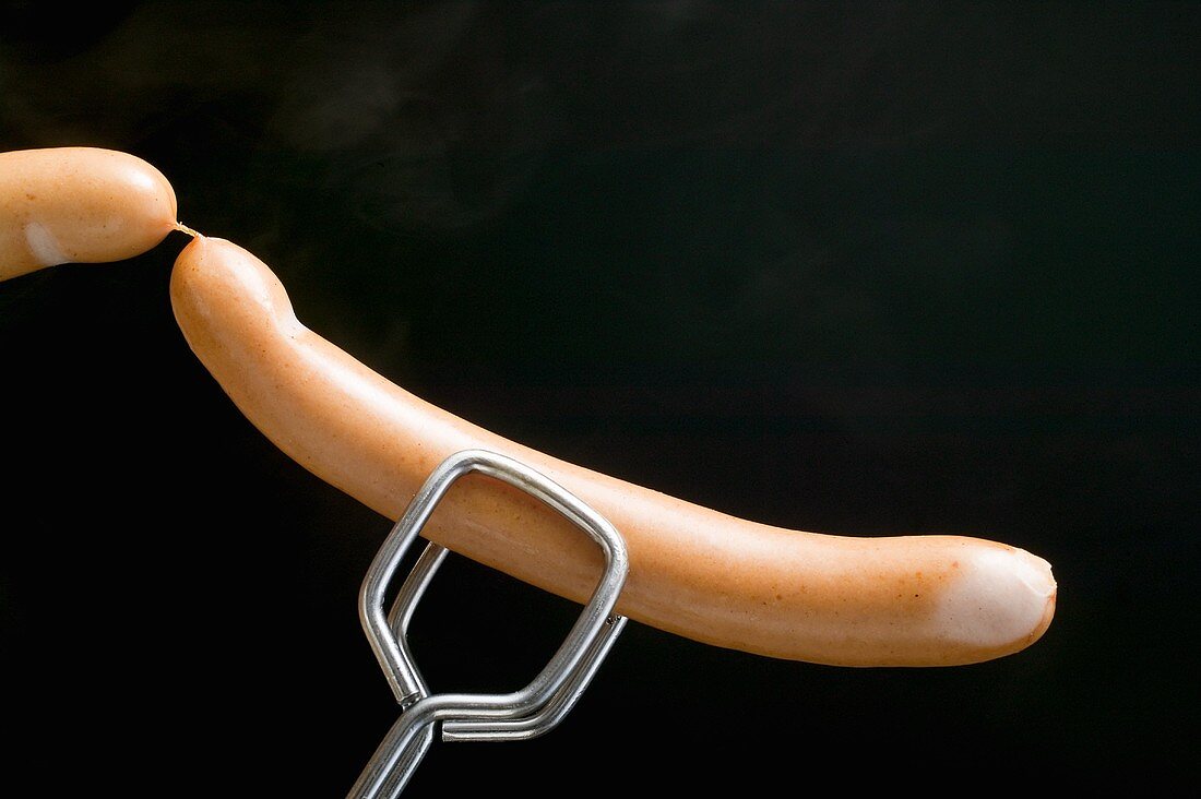 Tongs holding frankfurters