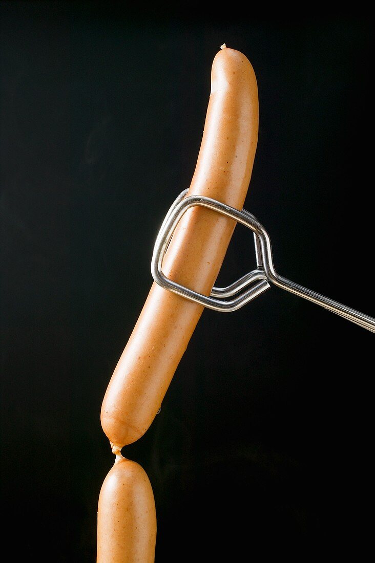 Tongs holding frankfurters