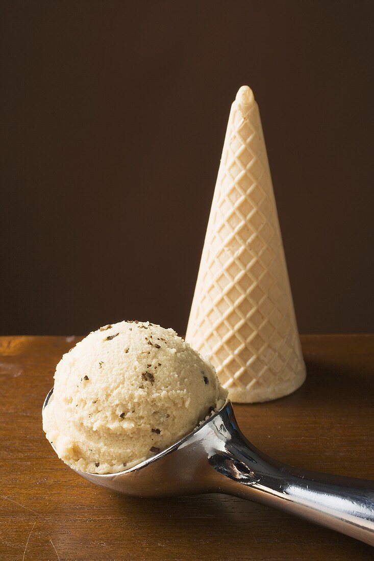 Scoop of ice cream in ice cream scoop, ice cream cone behind