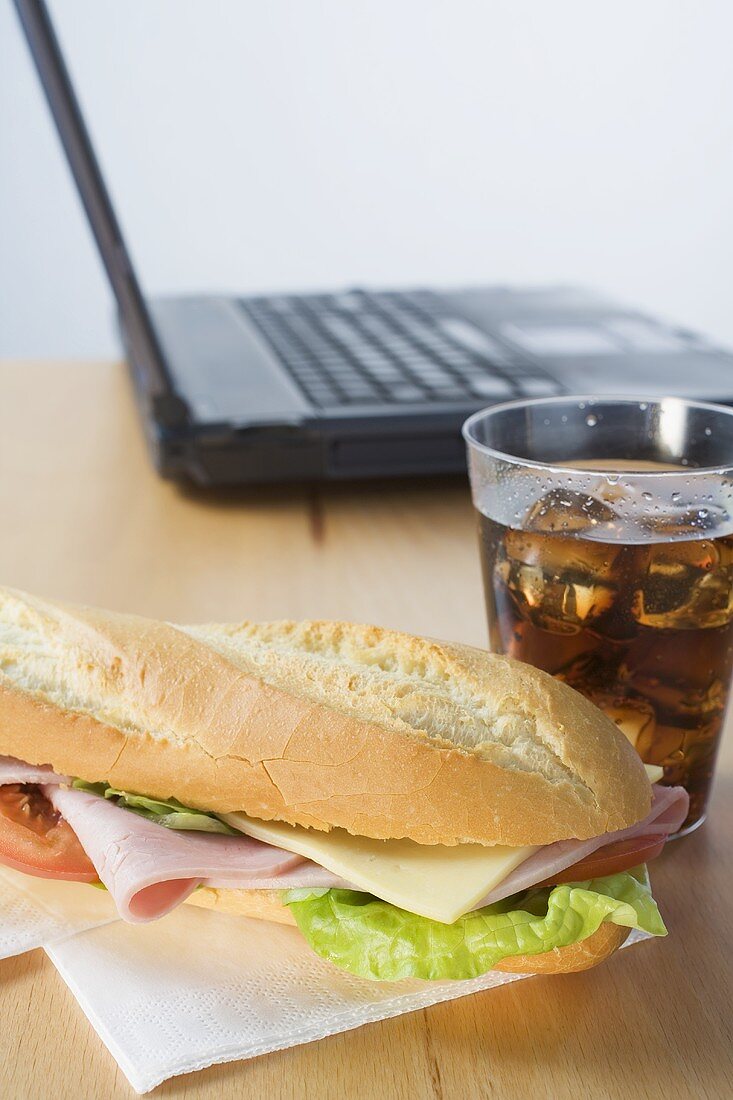 Sub sandwich and cola in front of laptop