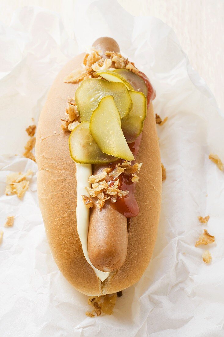 Hot dog with gherkin, mayonnaise & ketchup (overhead view)
