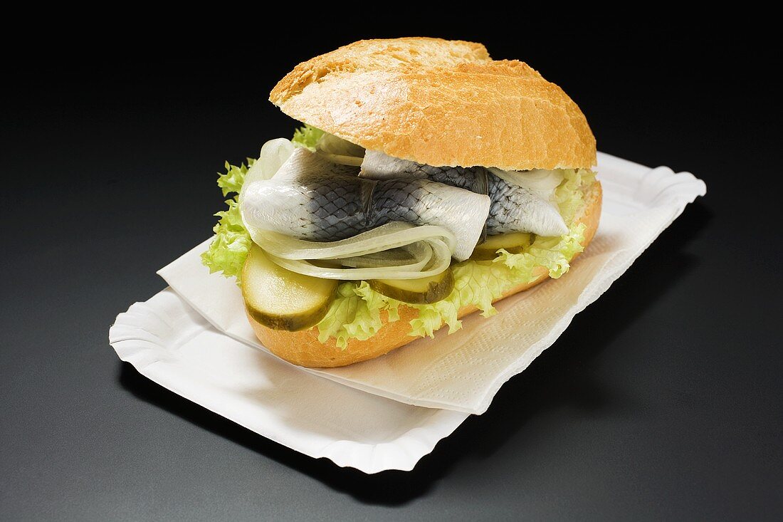 Herring, onions and gherkins in bread roll on paper plate