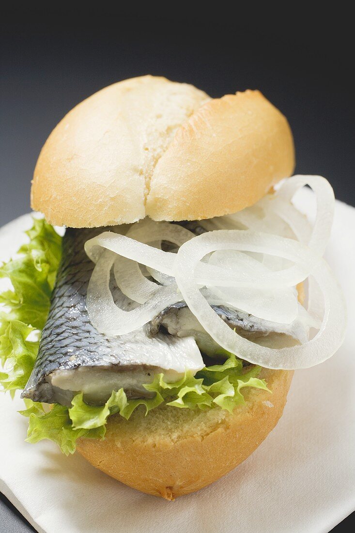 Bread roll filled with herring and onions on paper napkin