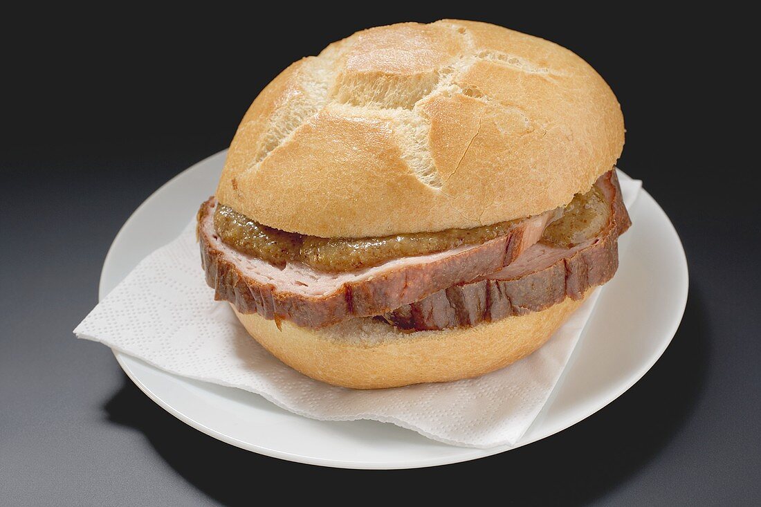 Leberkäse and mustard in roll on paper napkin on plate