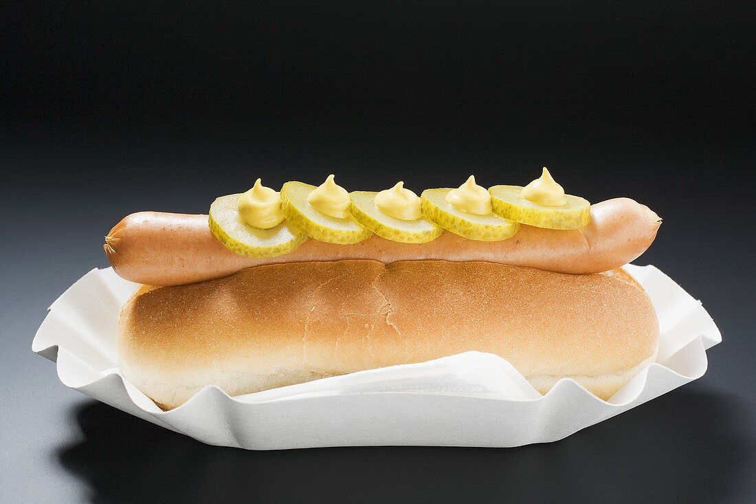 Hot dog with gherkins and mustard in paper dish