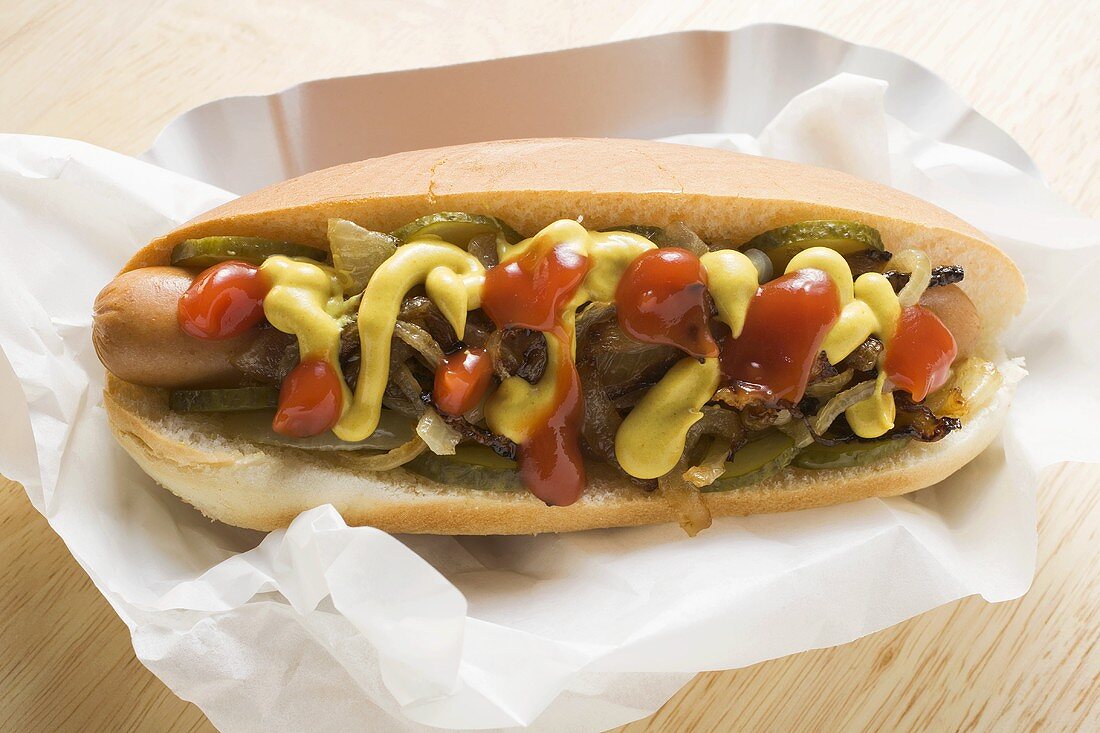 Hot dog with mustard, ketchup, gherkins and onions