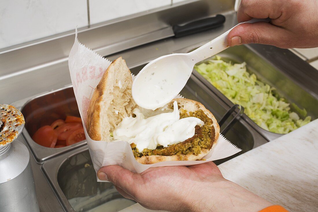 Adding yoghurt to pita bread filled with falafel