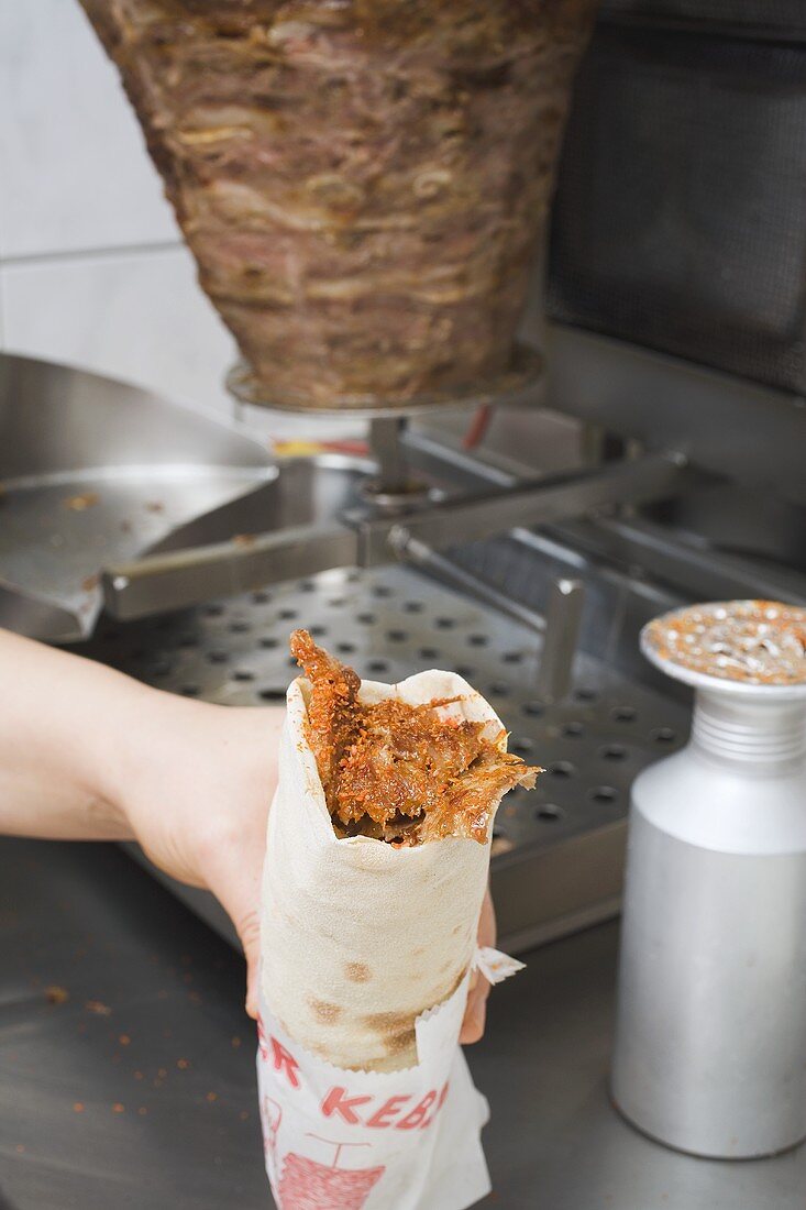 Hand hält Döner-Wrap im Imbisslokal