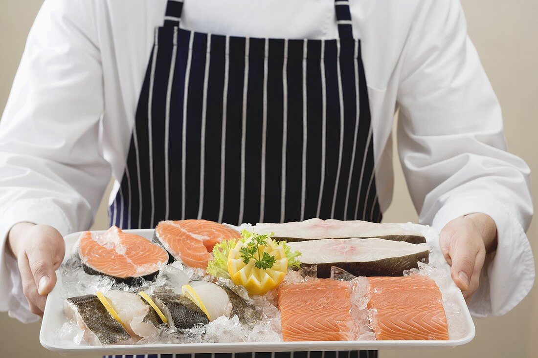 Person holding tray of salmon and sea bass pieces on ice