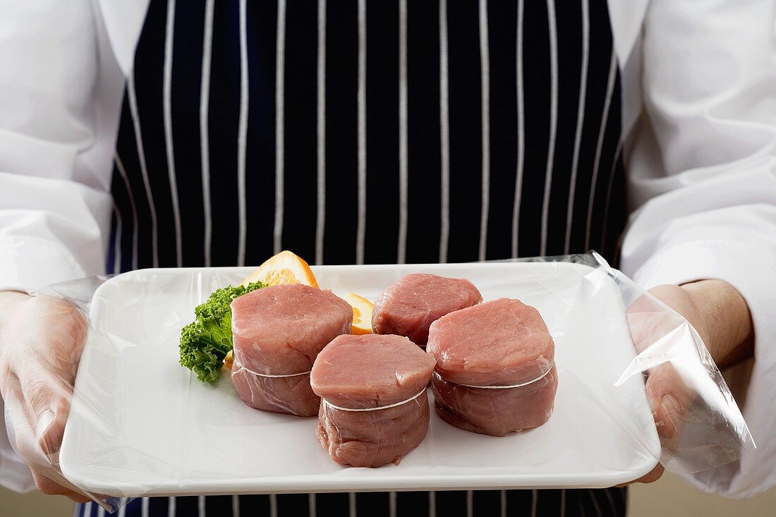 Person holding tray of pork medallions