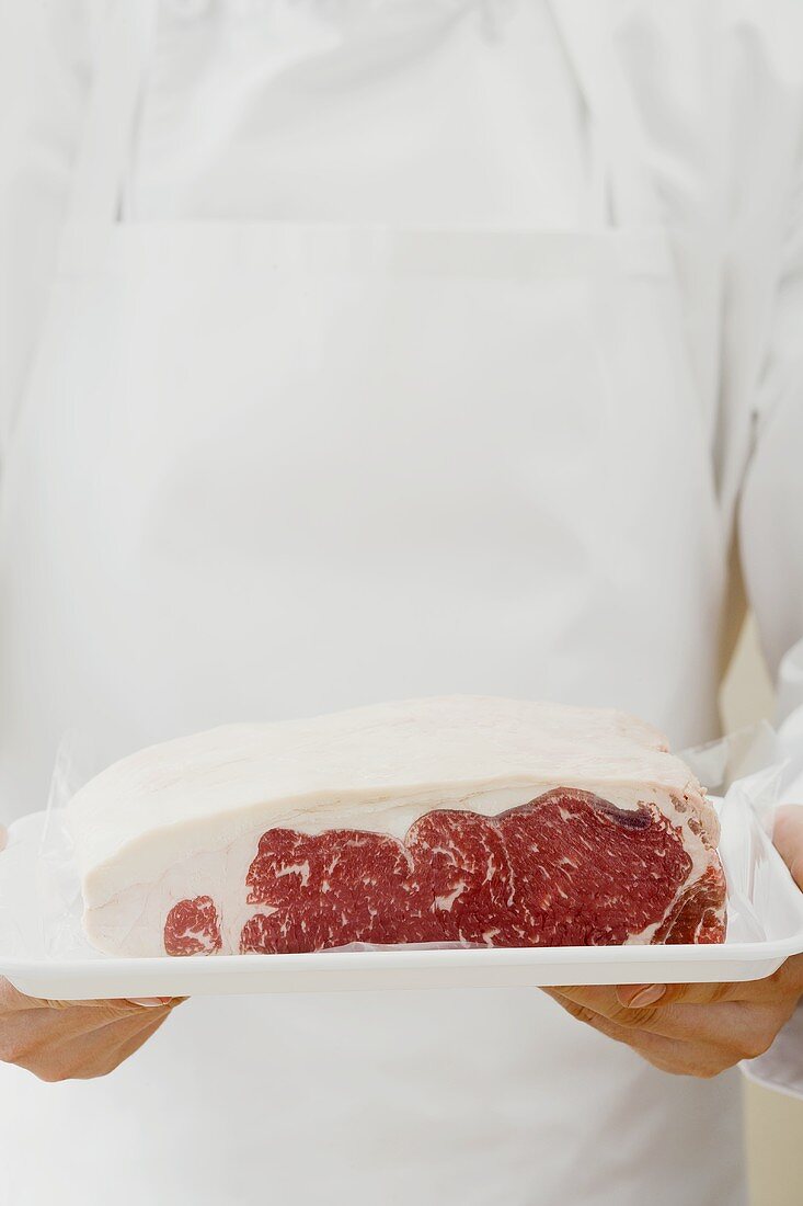 Person holding sirloin steak on tray