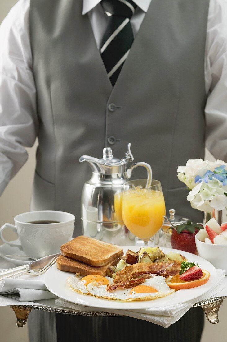 Butler serviert Frühstückstablett mit Bacon, Spiegelei, Toast