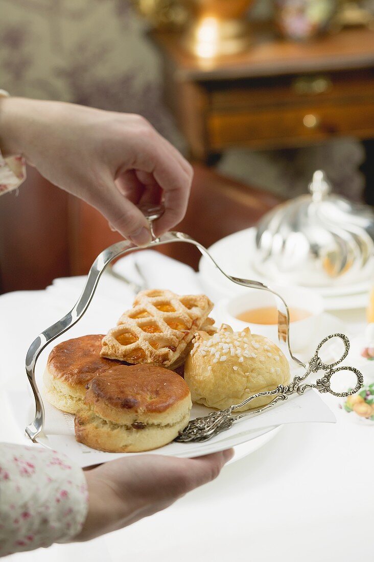 Hands serving sweet pastries and scones to eat with tea