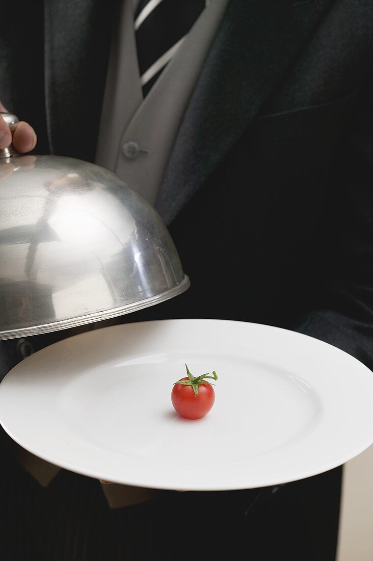 Butler serving cherry tomato on plate with dome cover