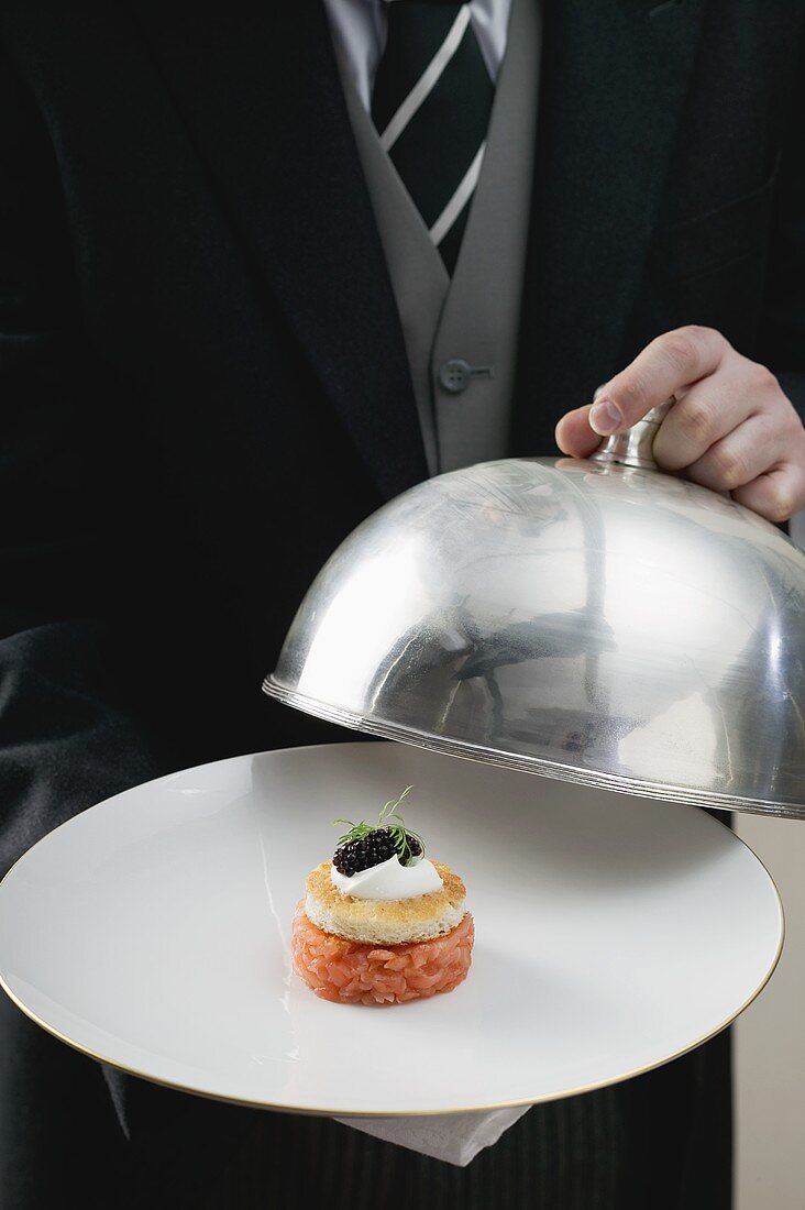 Butler serving salmon tartate on plate with dome cover