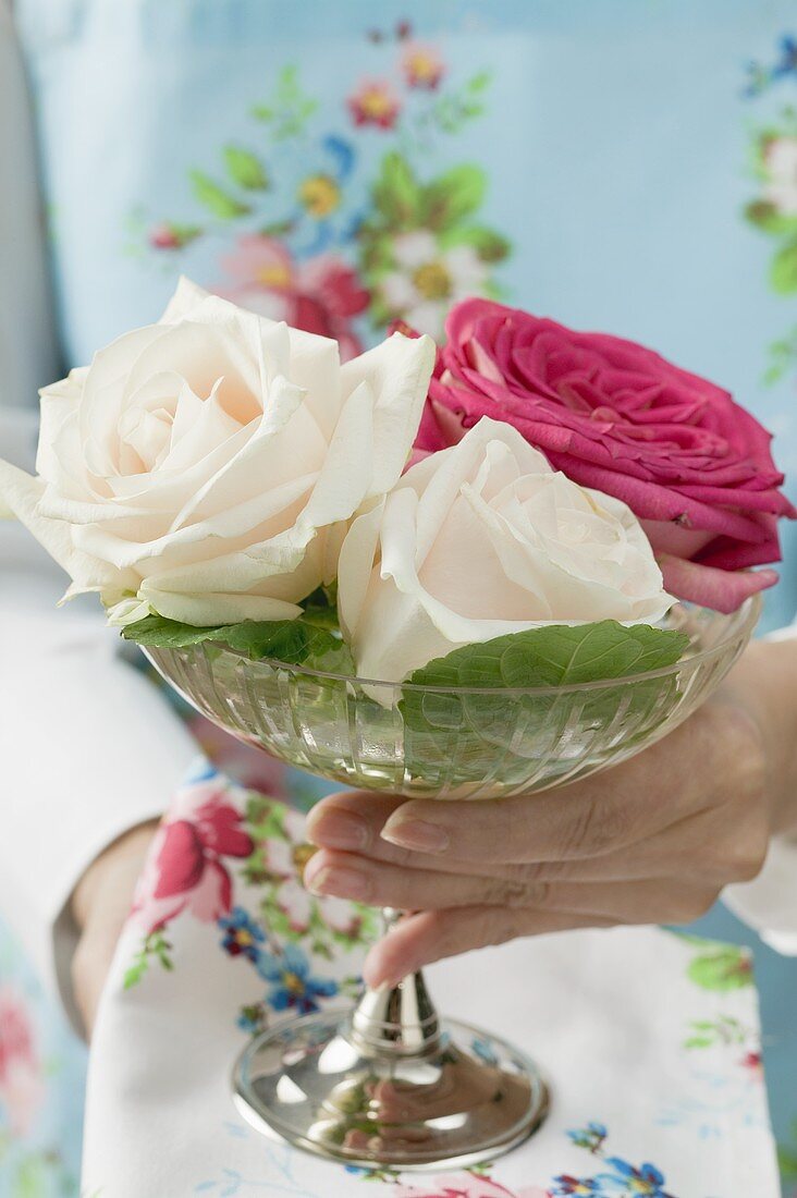 Frau hält Glassschale mit drei Rosen