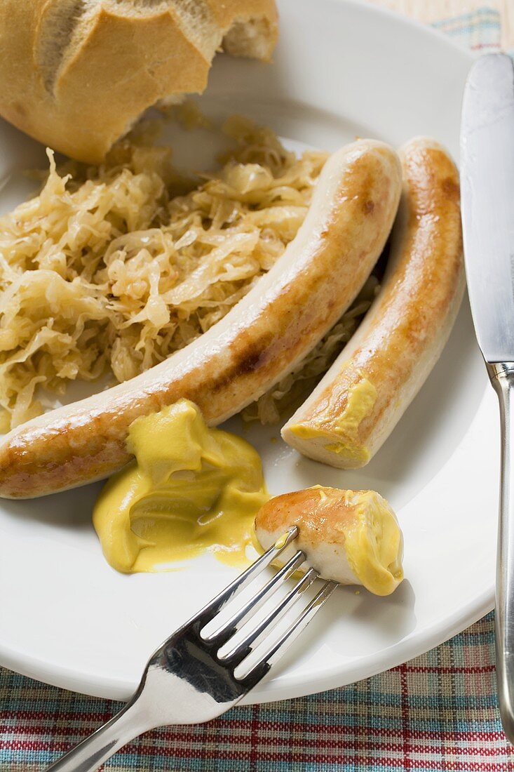 Grillwürste mit Sauerkraut, Senf und Brötchen (angebissen)