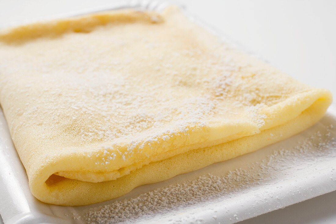 Crêpe with icing sugar on paper plate (close-up)