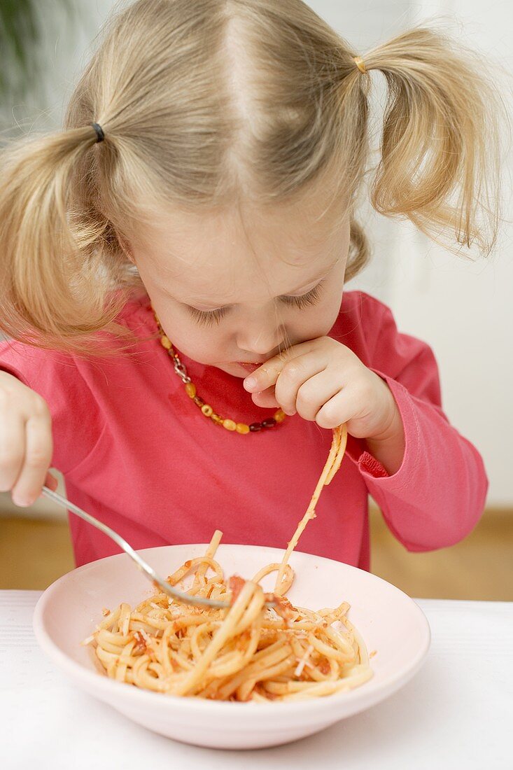 Small girl eating noodles with tomatoes