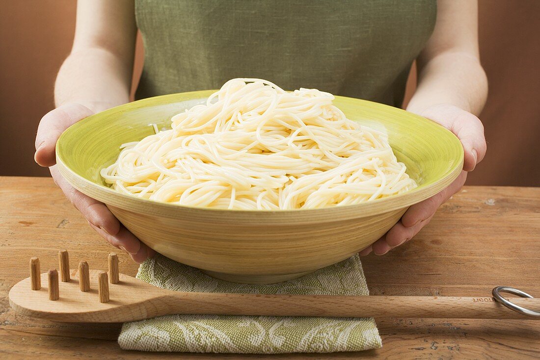 Woman holding bowl of cooked spaghetti