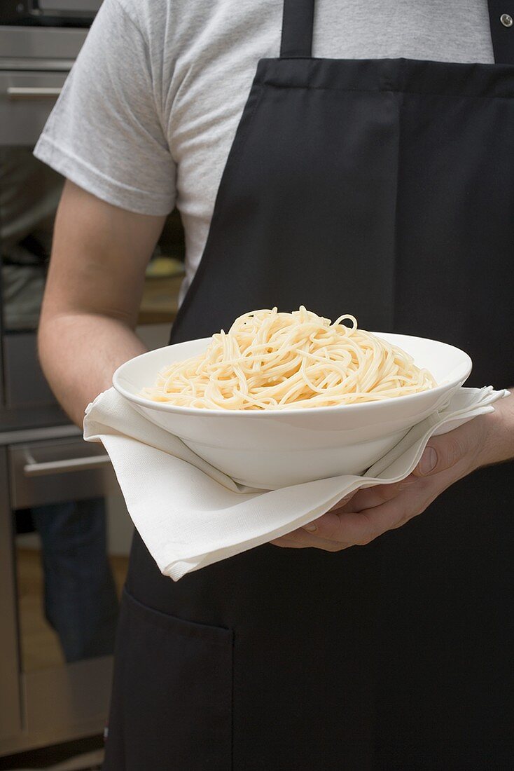 Person holding bowl of cooked spaghetti