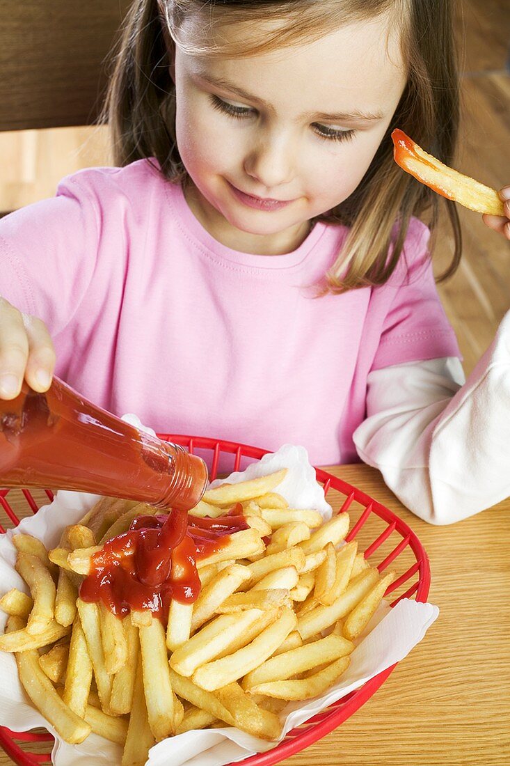 Mädchen schüttet Ketchup auf Pommes frites