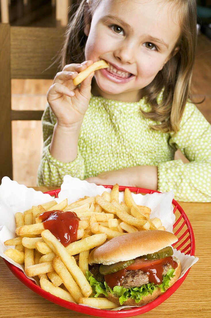 Mädchen isst Pommes frites mit Ketchup und Hamburger