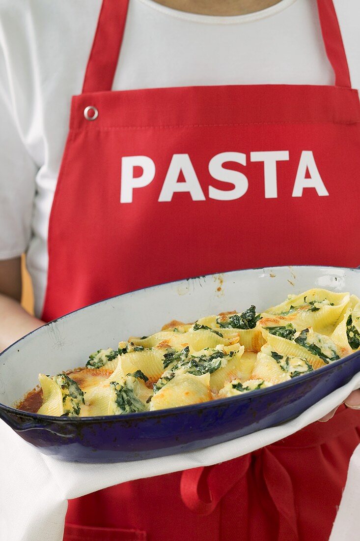 Woman in apron serving baked pasta dish
