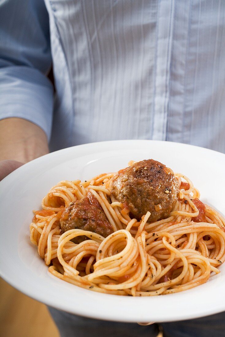 Person holding plate of spaghetti with meatballs