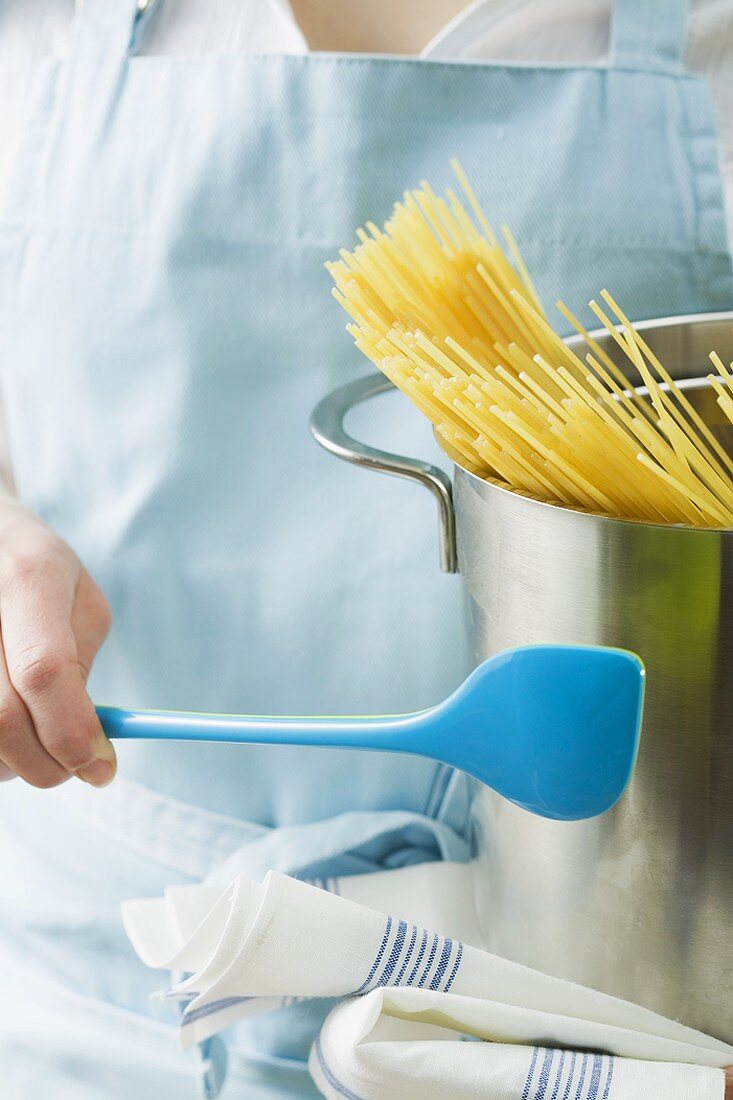 Woman holding kitchen spoon and pan with spaghetti